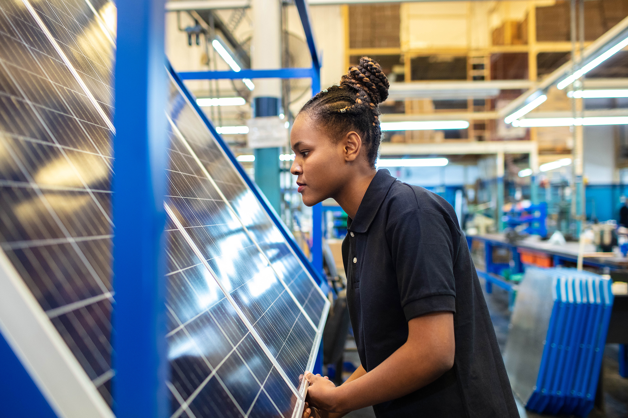 Young Black woman works on solar panel in factory.