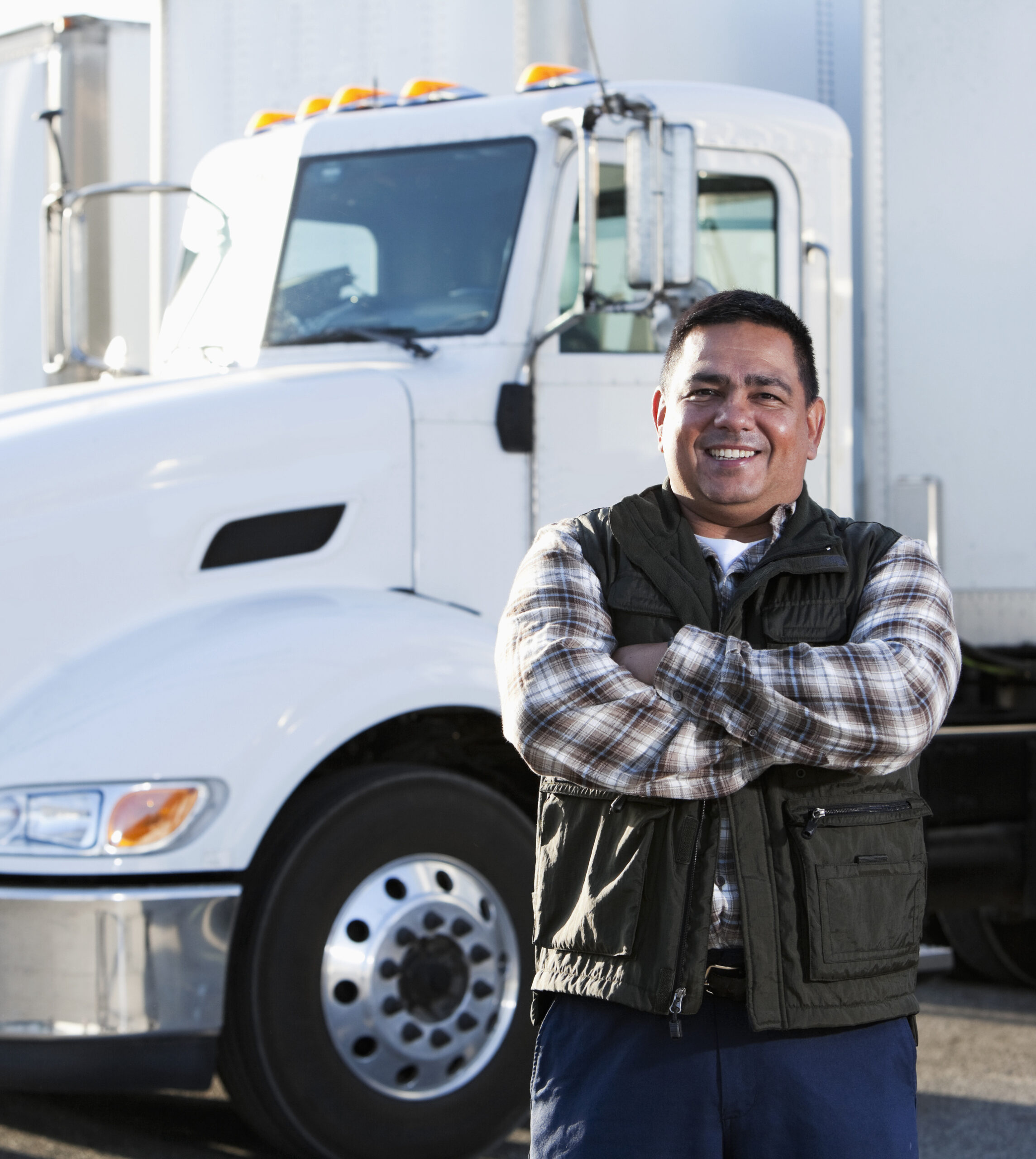 Latino man smiles proudly in front of semitruck
